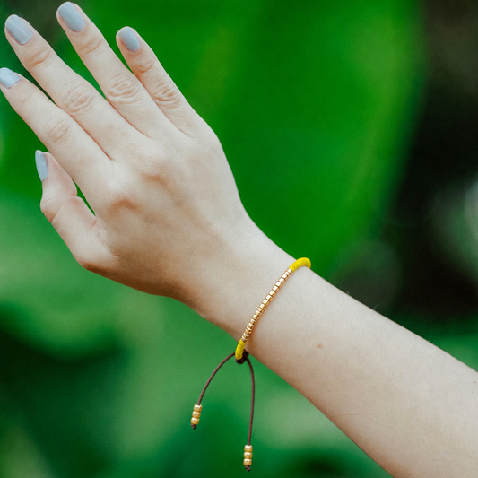 Hand wearing a yellow beaded bracelet against a blurred green background